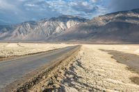 an empty road in front of a mountain range and dry, brown landscape with snow on it