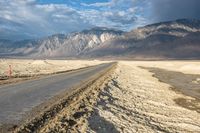 an empty road in front of a mountain range and dry, brown landscape with snow on it