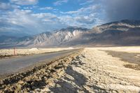 an empty road in front of a mountain range and dry, brown landscape with snow on it