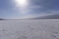 a large barren area with mountains in the distance and a bright sun over the horizon