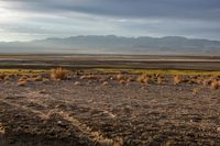 a desert landscape with mountains in the background and dirt on the ground at sunset time