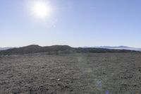 a lone field in an open area with sun on the horizon and mountains behind it