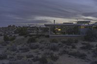 a modern house in the desert sits on a hilltop with desert scrubs in the foreground