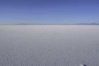 an empty dry salt plain with hills in the background with a snow covered area that has a bright, sundialed sky