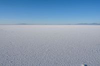 white snow on the ground in a large area with mountains and a blue sky behind