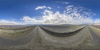 a wide angle image showing the road and a sky view with clouds in it in a desert area