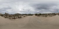 a dirt road going across desert with clouds in the distance of the image behind it