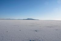 an open area with some mountains in the distance, with a few footprints in the sand