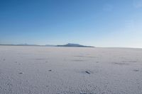 an open area with some mountains in the distance, with a few footprints in the sand