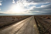 a rural road going through the desert at sunset or sunrises with mountains in the distance