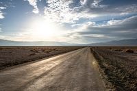 a rural road going through the desert at sunset or sunrises with mountains in the distance