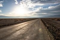 a rural road going through the desert at sunset or sunrises with mountains in the distance