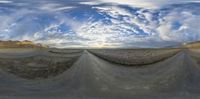 a 360 - lens panoramic view of a desert road under the cloudy sky