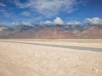 the view of an empty river flowing out of a dry lake bed in the desert, with mountains in the background