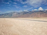 the view of an empty river flowing out of a dry lake bed in the desert, with mountains in the background