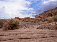 a dirt and rocky area surrounded by desert shrubbery under a cloudy blue sky,