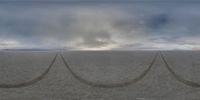 three tire tracks in a desert, while some clouds are rising above them and some mountains