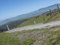 a motorcycle on a dirt road surrounded by hills and green grass on a clear day