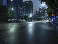 wet roadway with city buildings in the background at night with street lights on and no cars
