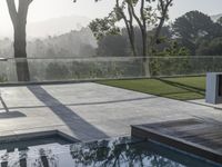 a patio with large windows overlooking the trees and an expansive swimming pool in the foreground