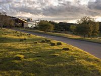 a dirt road that leads to a grassy area and a home with trees on it