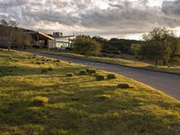 a dirt road that leads to a grassy area and a home with trees on it