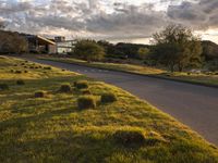 a dirt road that leads to a grassy area and a home with trees on it