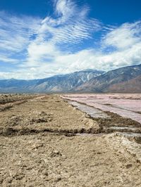 a dry lake and mountains surrounded by sand on a cloudy day on the horizon is an icy pink lagoon