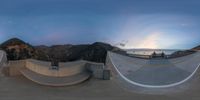 a wide angle photo of two skate boards at dusk in front of the ocean and mountains