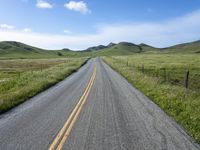 a long empty road surrounded by hills under a blue sky is in the foreground