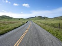 a long empty road surrounded by hills under a blue sky is in the foreground