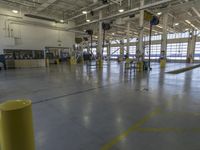 a large warehouse with various equipment on the floor and yellow pillars and doors in the middle of it
