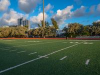 an empty football field with several players running in it and a view of buildings and trees