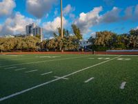 an empty football field with several players running in it and a view of buildings and trees