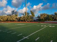 an empty football field with several players running in it and a view of buildings and trees