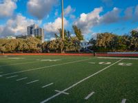 an empty football field with several players running in it and a view of buildings and trees