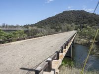 a view from a bridge overlooking trees and a mountain range of hills behind a bridge