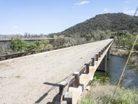 a view from a bridge overlooking trees and a mountain range of hills behind a bridge