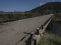 a view from a bridge overlooking trees and a mountain range of hills behind a bridge