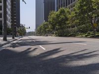 an empty street with tall buildings in the background and trees on both sides of the road