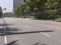 an empty street with tall buildings in the background and trees on both sides of the road