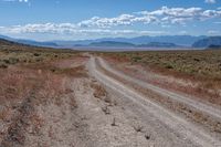 dirt road in an arid field with mountains in background at daytime with cloudy blue skies