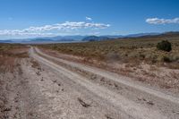 dirt road in an arid field with mountains in background at daytime with cloudy blue skies