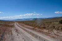 dirt road in an arid field with mountains in background at daytime with cloudy blue skies