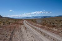 dirt road in an arid field with mountains in background at daytime with cloudy blue skies