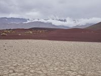 a cow is walking across the barren ground under stormy skies above mountains and clouds are low