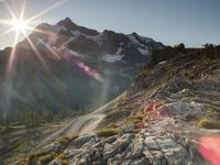 a mountain view with the sun peaking over the top of the mountain range and the road in front