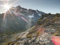 a mountain view with the sun peaking over the top of the mountain range and the road in front