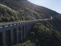 a car driving down the highway by a mountain side highway bridge with grass growing on the edge