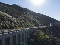 a car driving down the highway by a mountain side highway bridge with grass growing on the edge